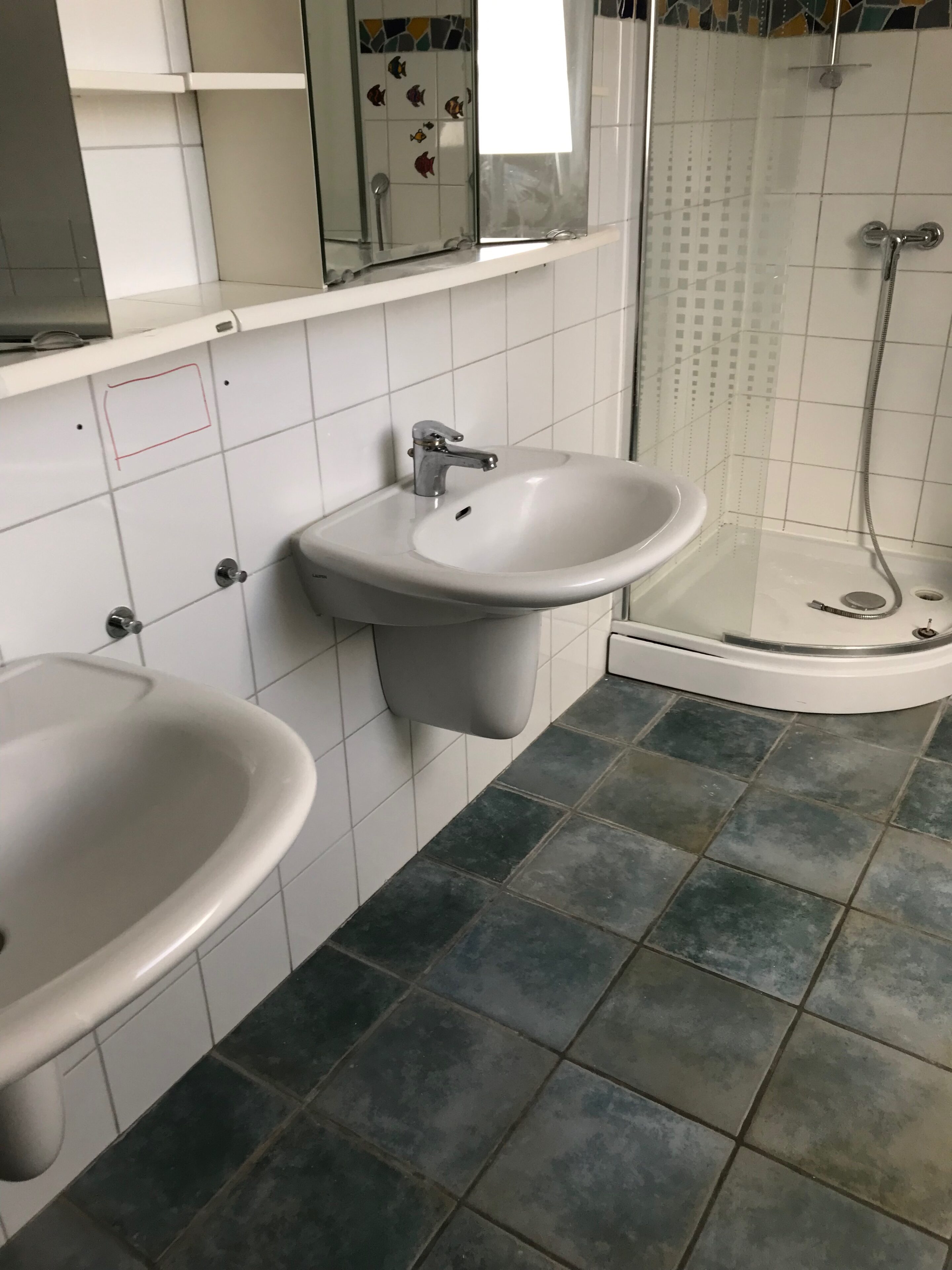 Altes Badezimmer mit gefliesten Wänden und enger Duschkabine vor der Sanierung