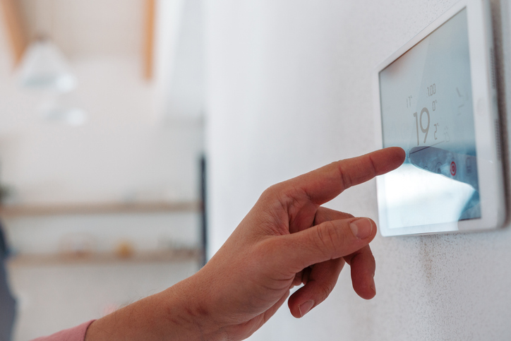 Hand stellt an einem digitalen Raumthermostat 19 Grad ein