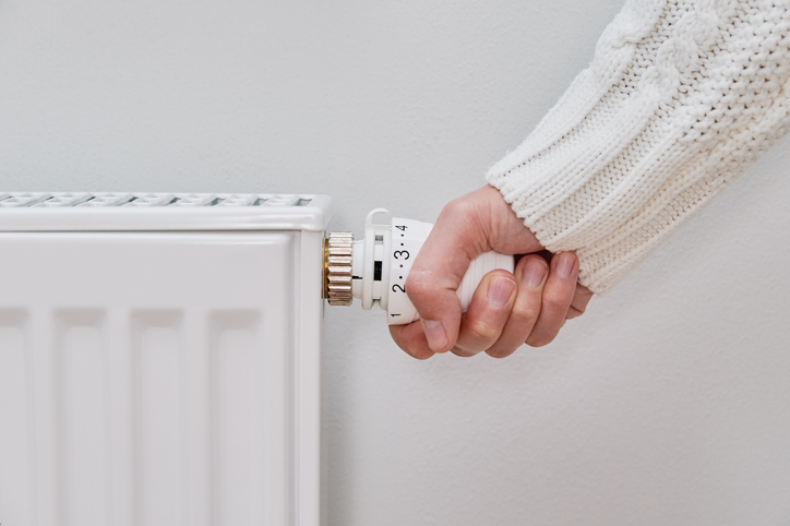 Hand stellt das Thermostatventil an einem weißen Heizkörper ein
