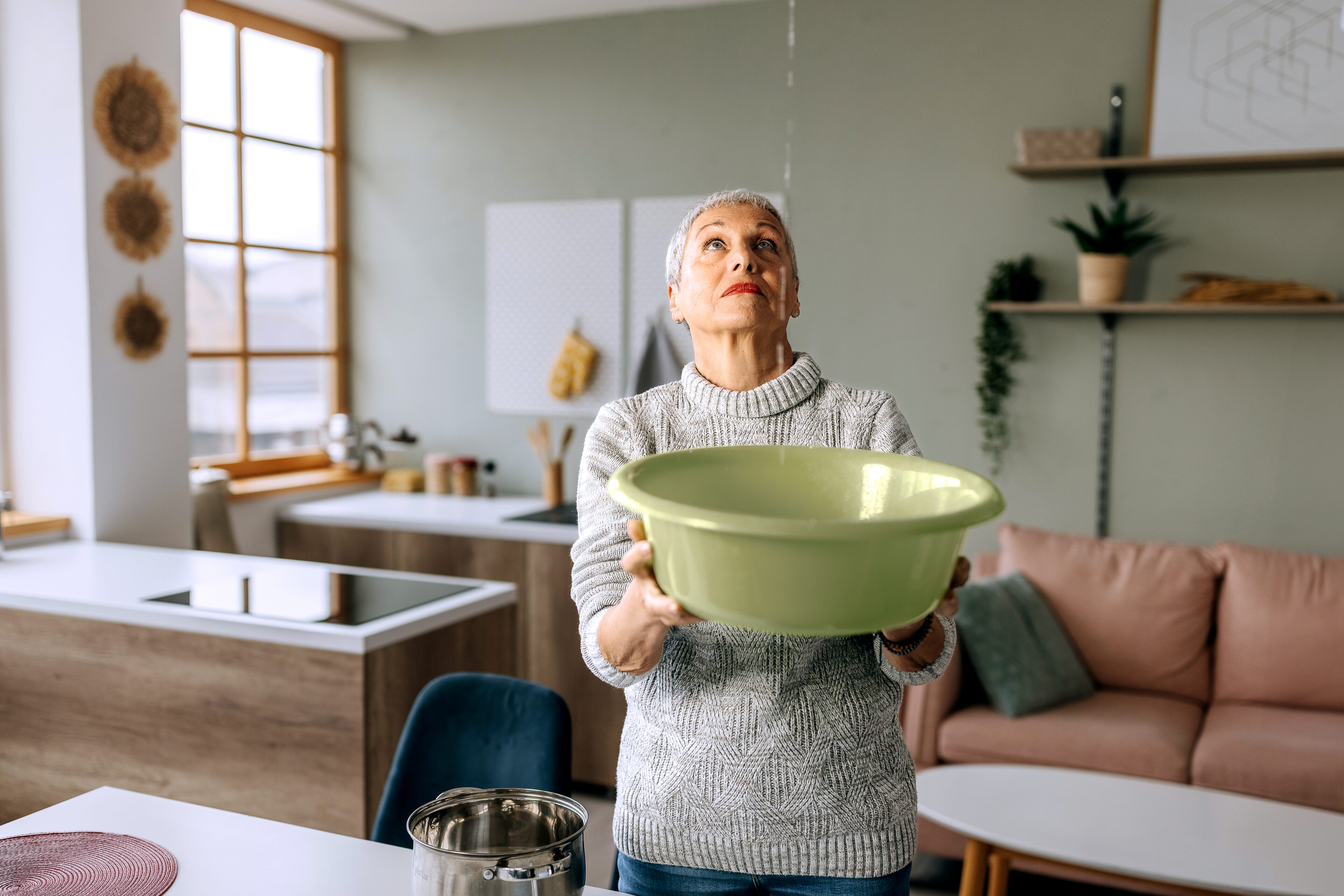 Frau fängt mit einer Schüssel Wasser auf, das von der Decke tropft