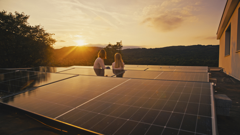 Zwei Personen sitzen bei Sonnenuntergang neben Photovoltaikmodulen auf einem Flachdach