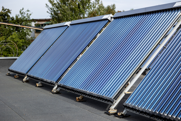 Vier Röhrenkollektoren einer Solarthermieanlage stehen aufgeständert auf einem Flachdach